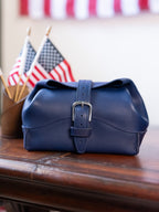 Saddleback Club Membership George Washington Leather Roll-Up Toiletry Bag in Blue on a wood desk with flags and bunting behind