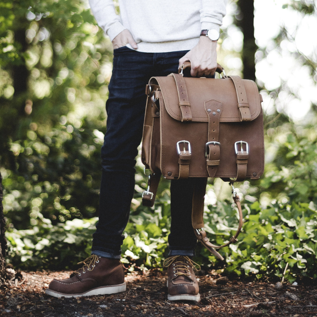Man in a forest holding a brown Classic Leather Briefcase with detachable backpack straps