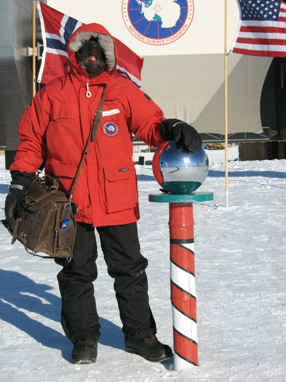 Person in polar gear carrying a large brown Classic Leather Briefcase at the South Pole marker