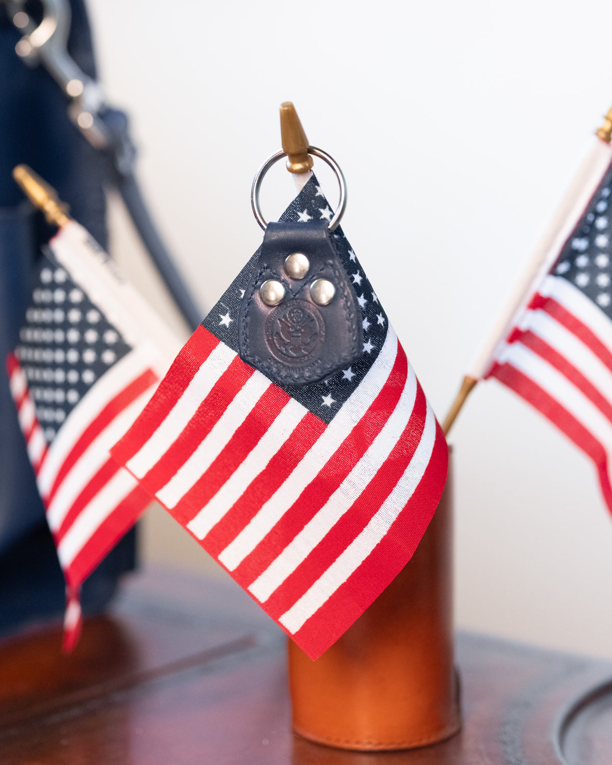 The navy leather keychain fob, embossed and riveted, hanging in front of two small United States flags