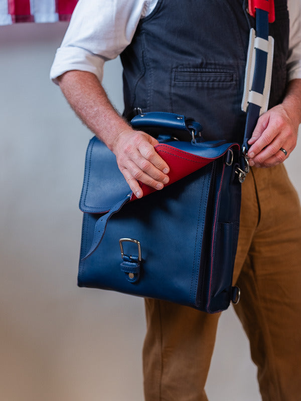 A man lifting the messenger bag's flap to show the red lining inside