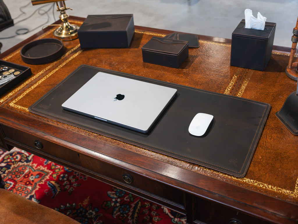 Long Desk Pad in Dark Coffee Brown on an antique wooden desk with a closed laptop, white mouse and leather boxes
