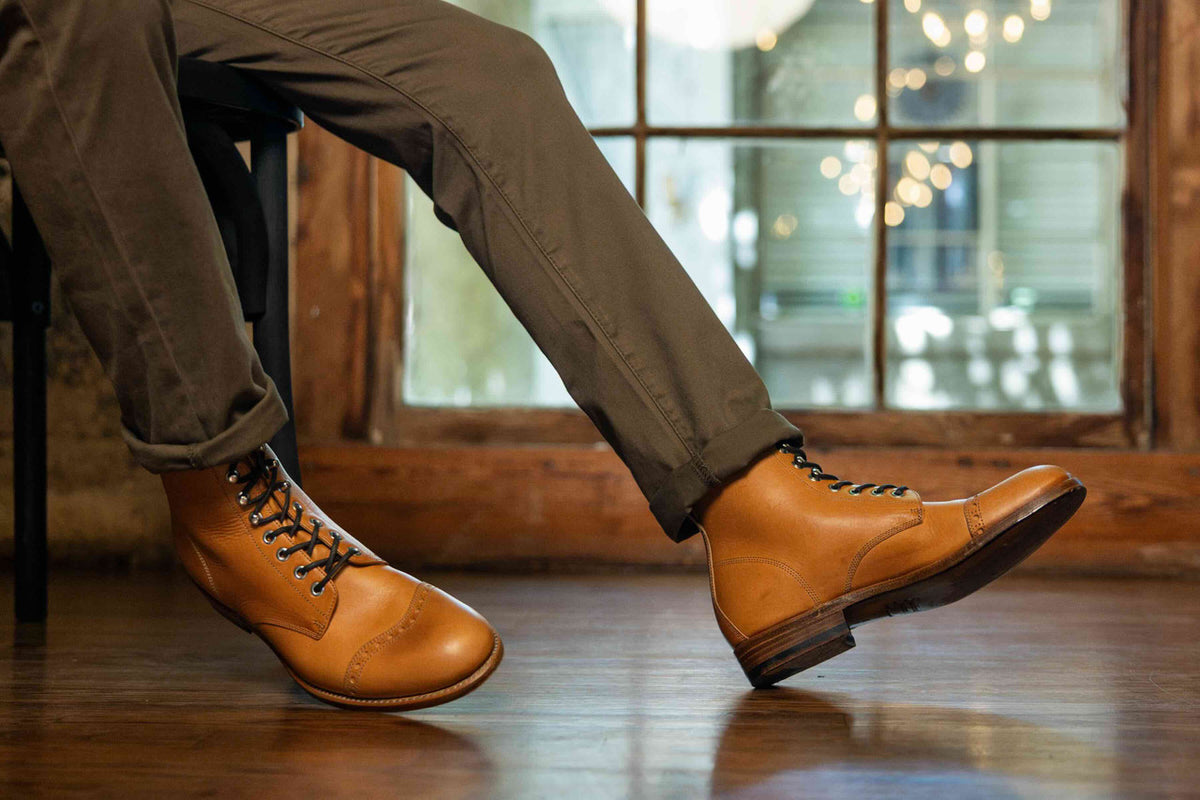 High quality English tan leather Officer's Boots worn with olive trousers while seated by a window, side view