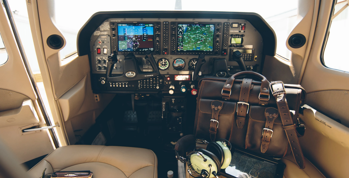 Dark brown Saddleback Leather Flight Bag on the floor of an airplane cockpit next to a pilot headset