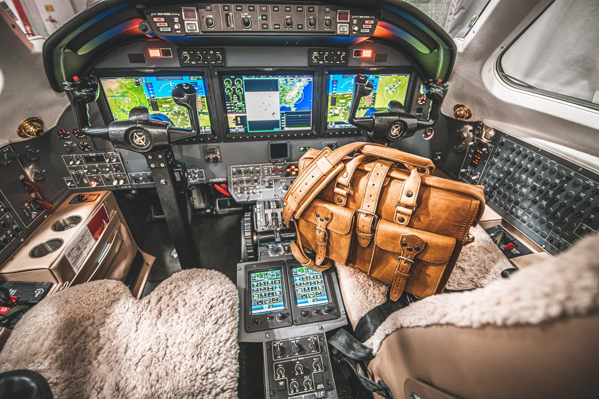 Tan leather Flight Bag briefcase on the copilot seat of a private jet cockpit with lit instrument panels