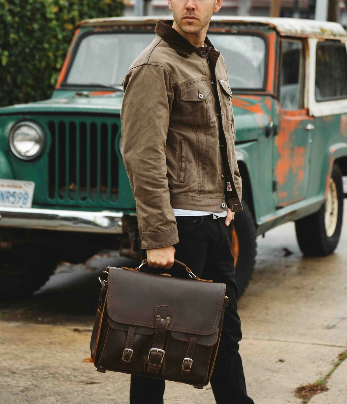 Man carrying a dark brown Front Pocket Leather Briefcase in front of a vintage teal truck