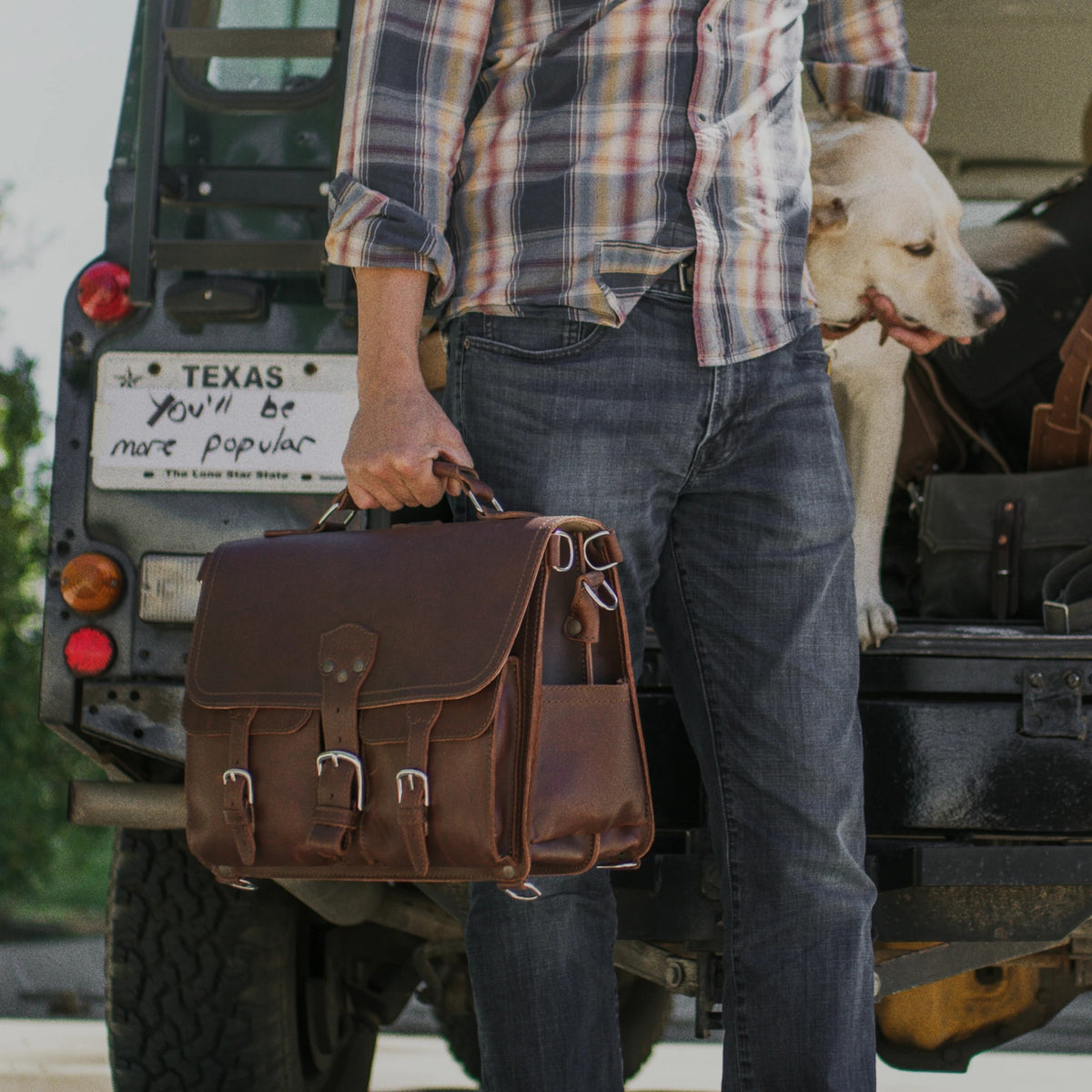 Man carrying a brown Front Pocket Leather Briefcase by the handle with a dog in the truck behind