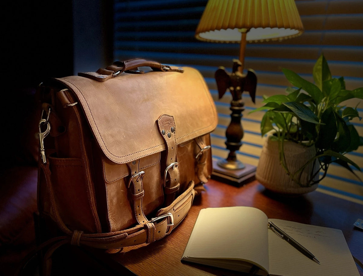 Front Pocket Leather Briefcase in brown on a desk beside a lamp, plant and open notebook