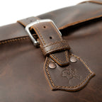 24" Waterbag in dark brown, close-up of a buckle strap and riveted tab with embossed pig logo