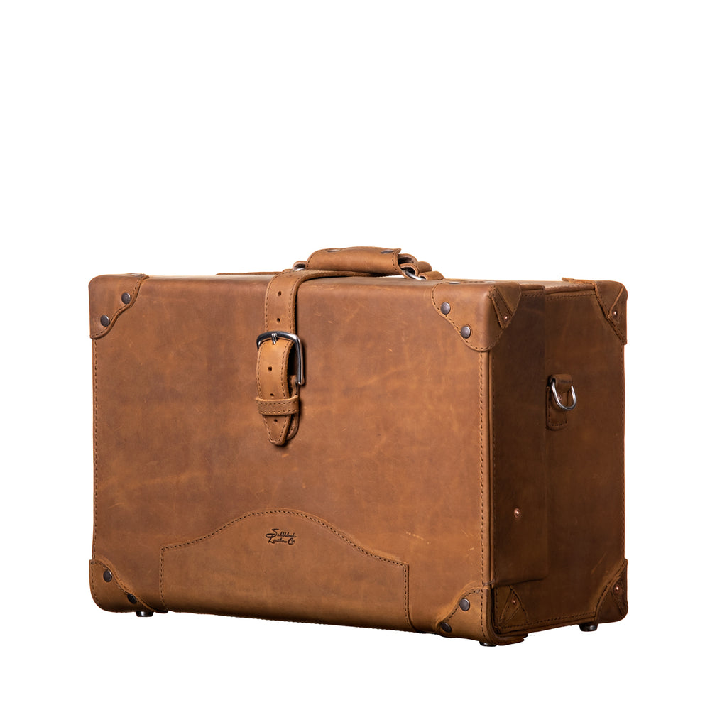 Grandfather Overnight Case in Tobacco, angled front view with top handle, buckled strap and metal corner caps