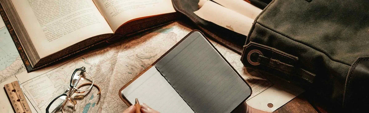 Leather notebook cover, open book, glasses and dark leather bag on a desk with a map