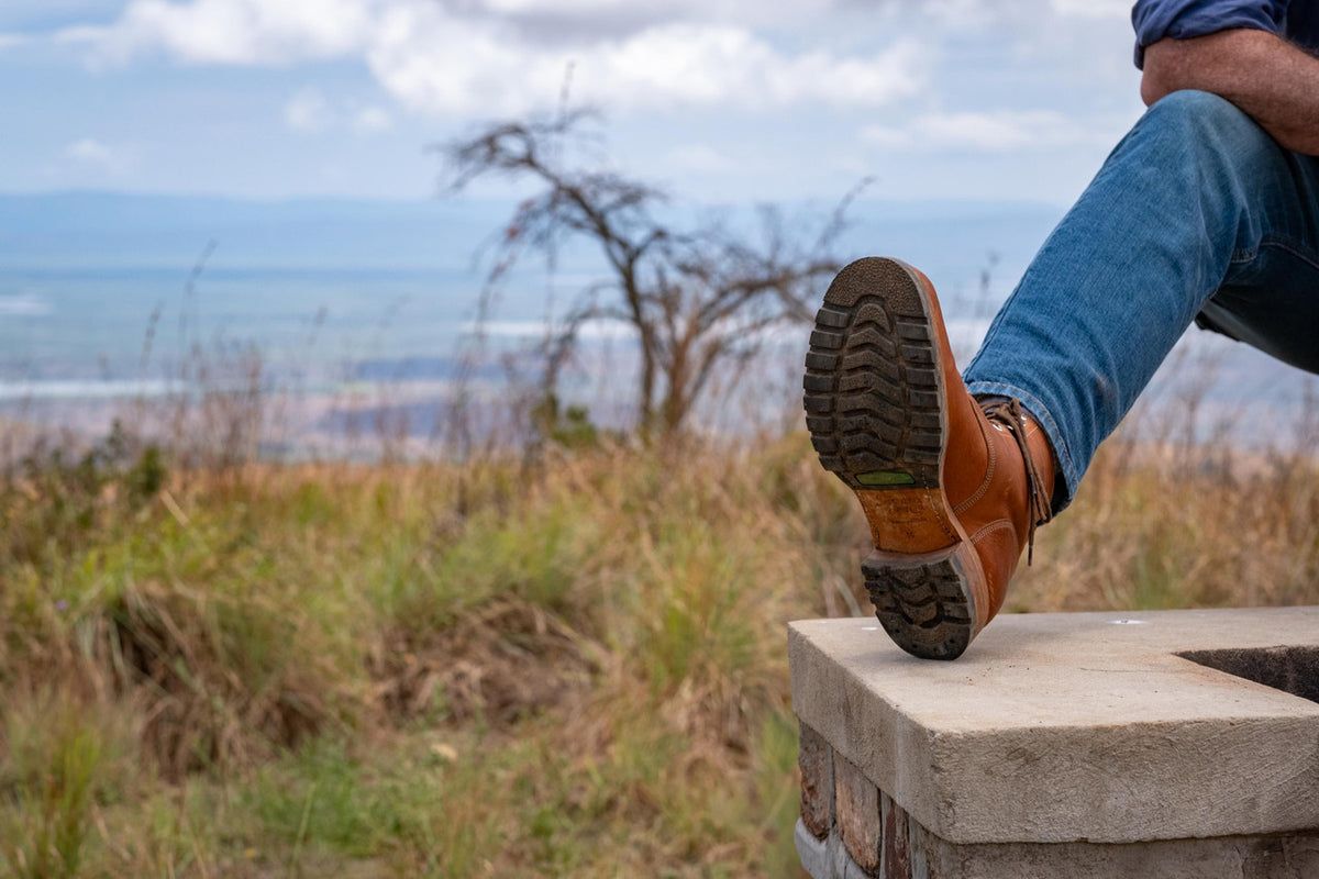 High quality natural tan leather Huntsman Boot stepping over a stone ledge, sole view of the lug tread