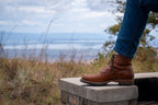 Huntsman Boots in brown leather, one boot on a stone post overlooking a grassy field and water