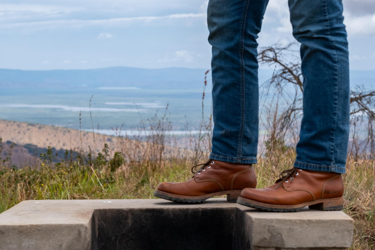 Huntsman Boots in brown leather, worn with jeans on a stone ledge overlooking hills and water