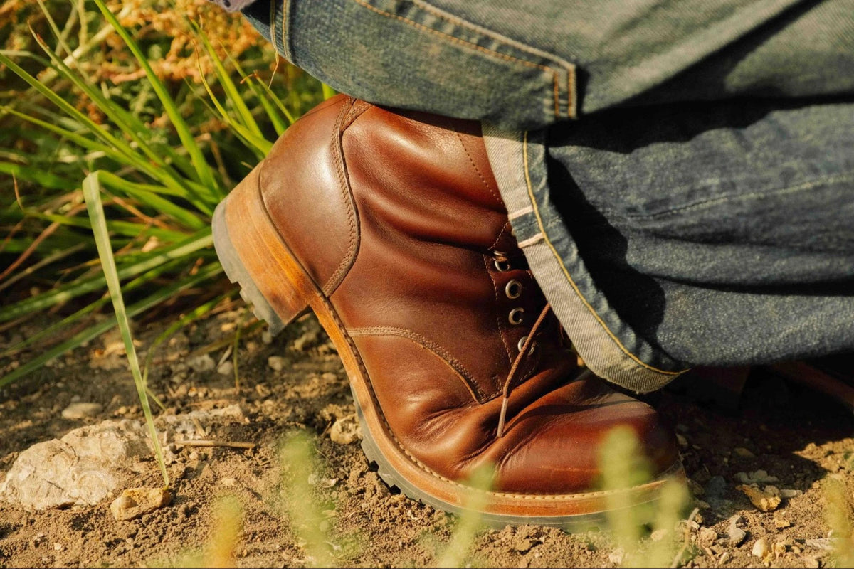 Huntsman Boots - Dark Coffee Brown on foot, close-up of the boot and jeans cuff in dry grass and dirt