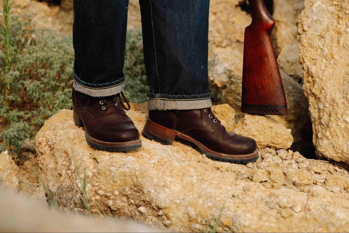 Huntsman Boots - Dark Coffee Brown on foot with cuffed dark jeans, standing on sunlit rocks