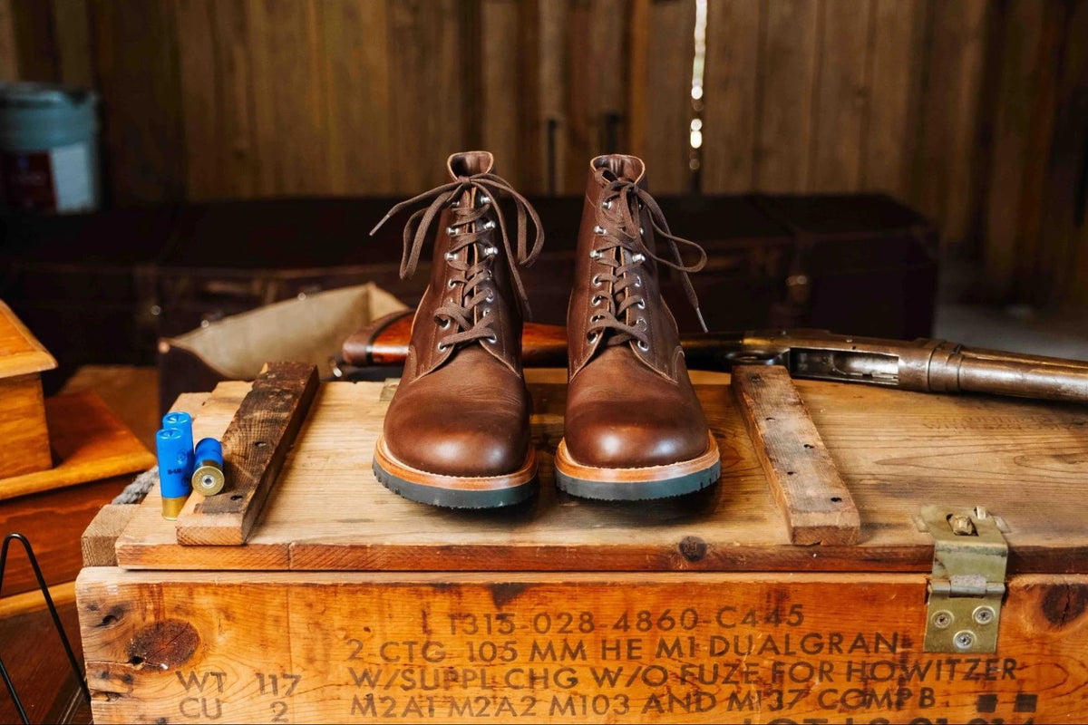 Huntsman Boots - Dark Coffee Brown, front view of a laced pair on a stenciled wooden crate in a rustic cabin