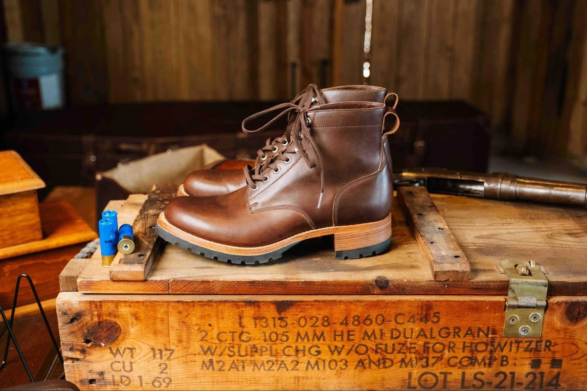 Huntsman Boots - Dark Coffee Brown, left side profile of a pair on a stenciled wooden crate in a rustic cabin