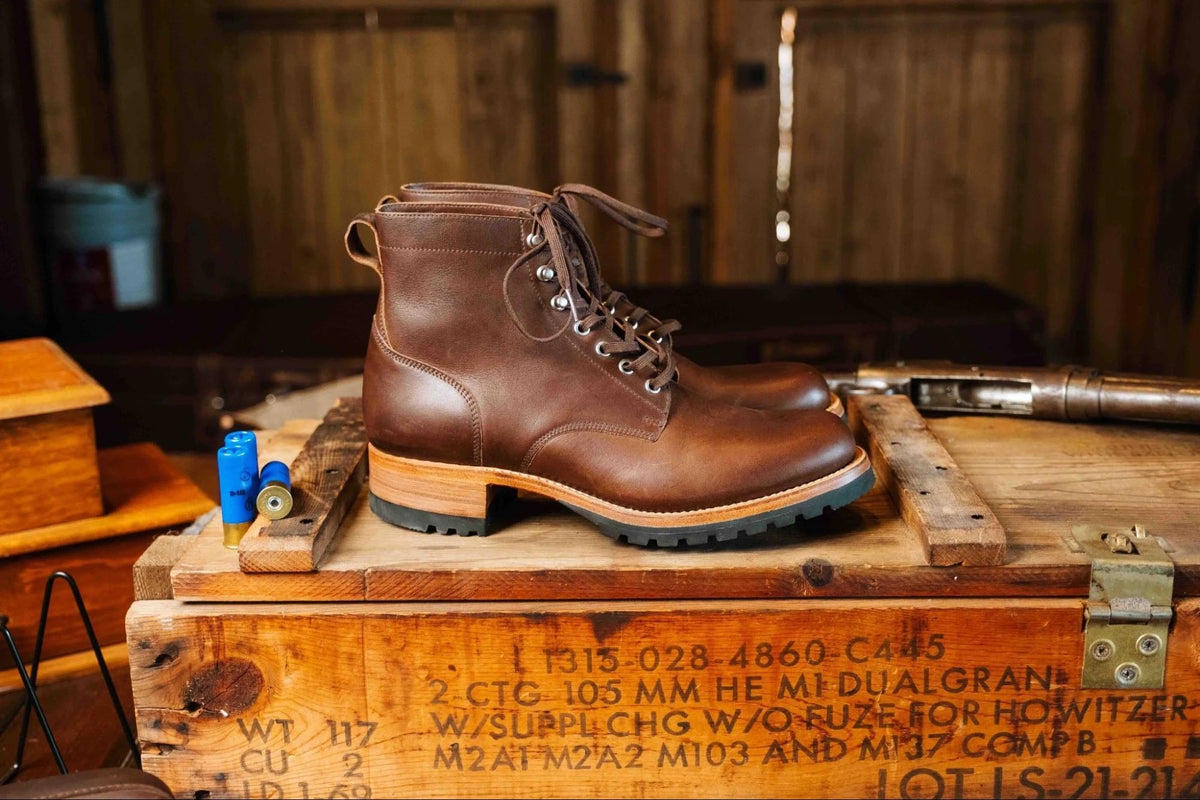 Huntsman Boots - Dark Coffee Brown, right side profile of a pair on a stenciled wooden crate in a rustic cabin