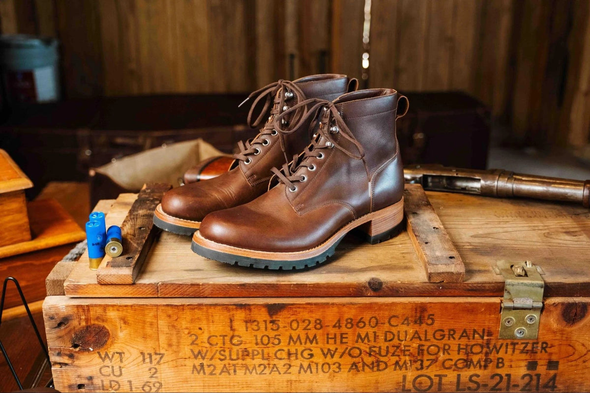 Huntsman Boots - Dark Coffee Brown, three-quarter view of a laced pair on a stenciled wooden crate in a rustic cabin