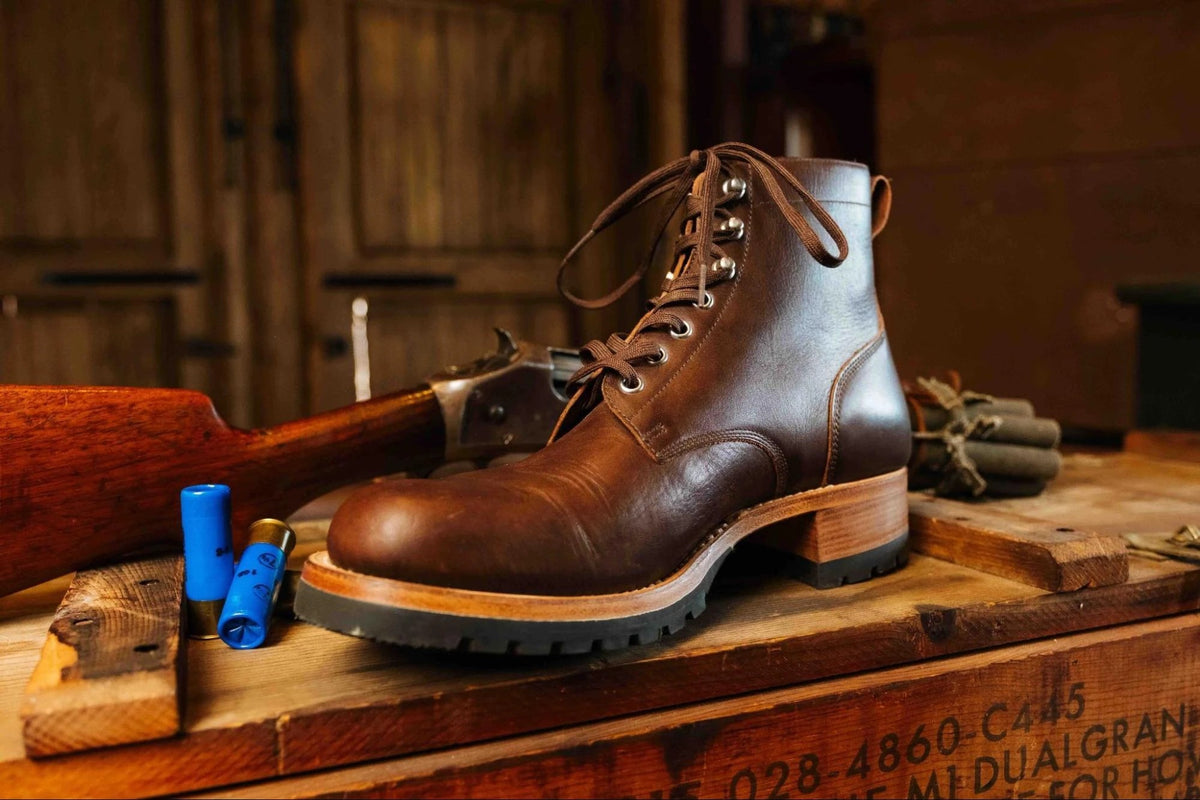 Huntsman Boots - Dark Coffee Brown, three-quarter view of one boot on a stenciled crate in a rustic barn