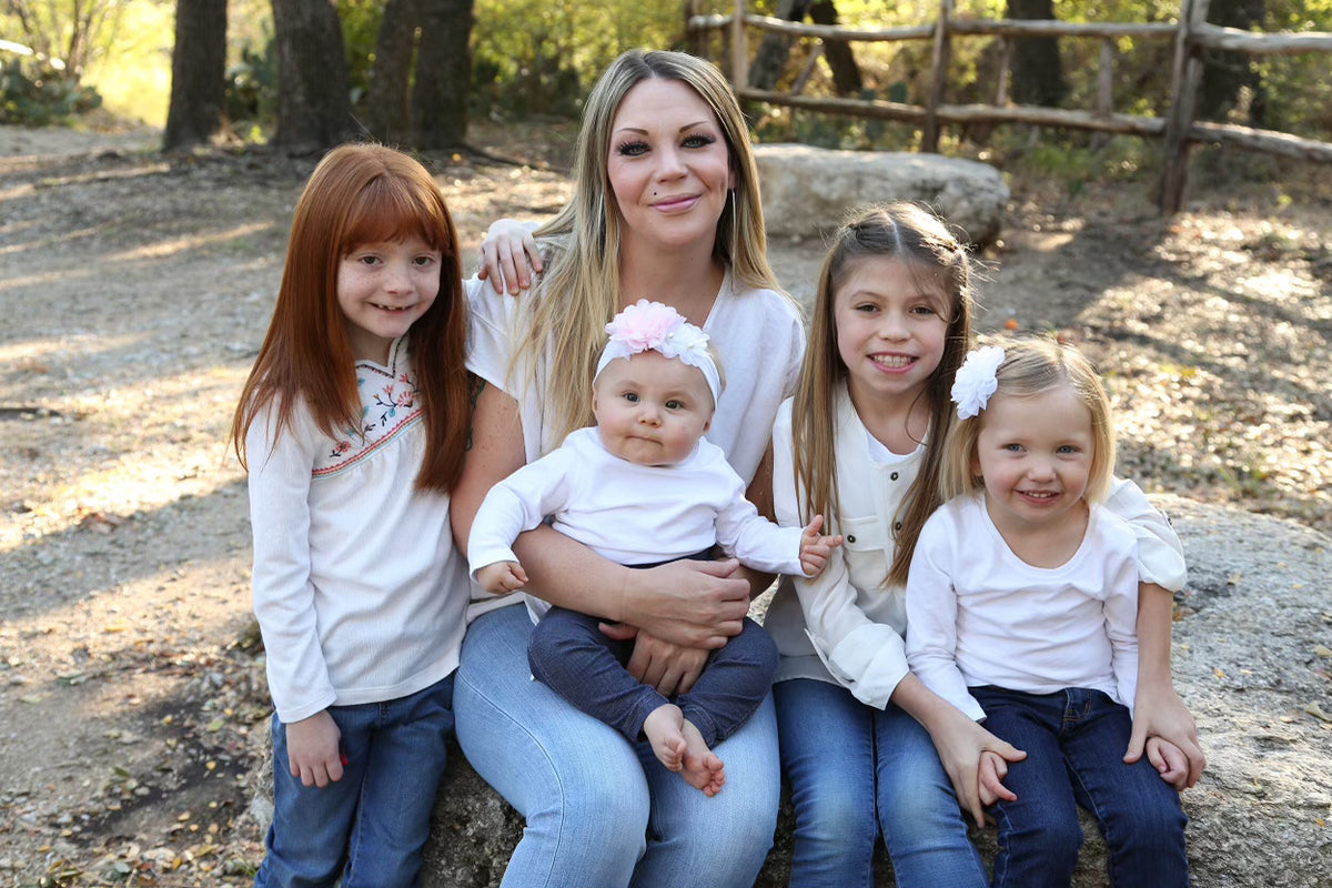 The same family outdoors in matching white tops, the four older children gathered around their mother holding the baby