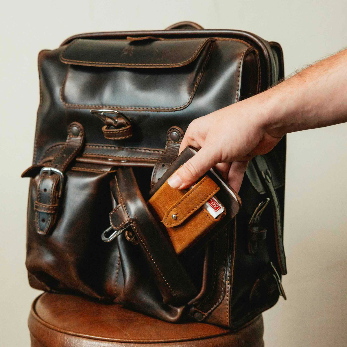 Big Mouth Leather Backpack in Dark Coffee Brown, a hand pulling a wallet from the front pocket