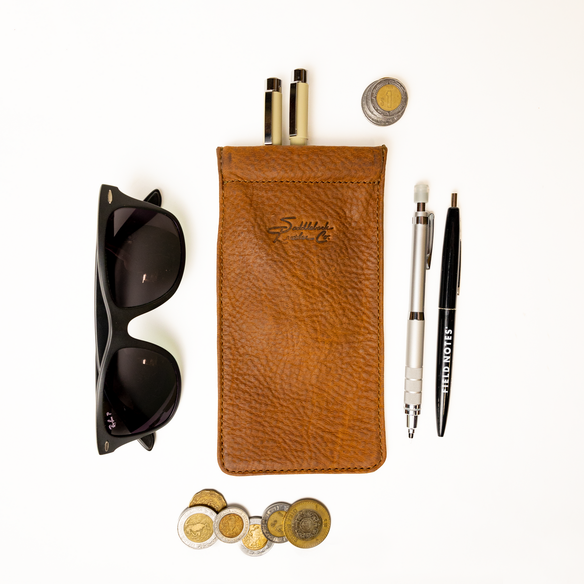 Bear Trap Leather Pen Case in Tobacco, flat lay with sunglasses, pens, a mechanical pencil and stacked coins