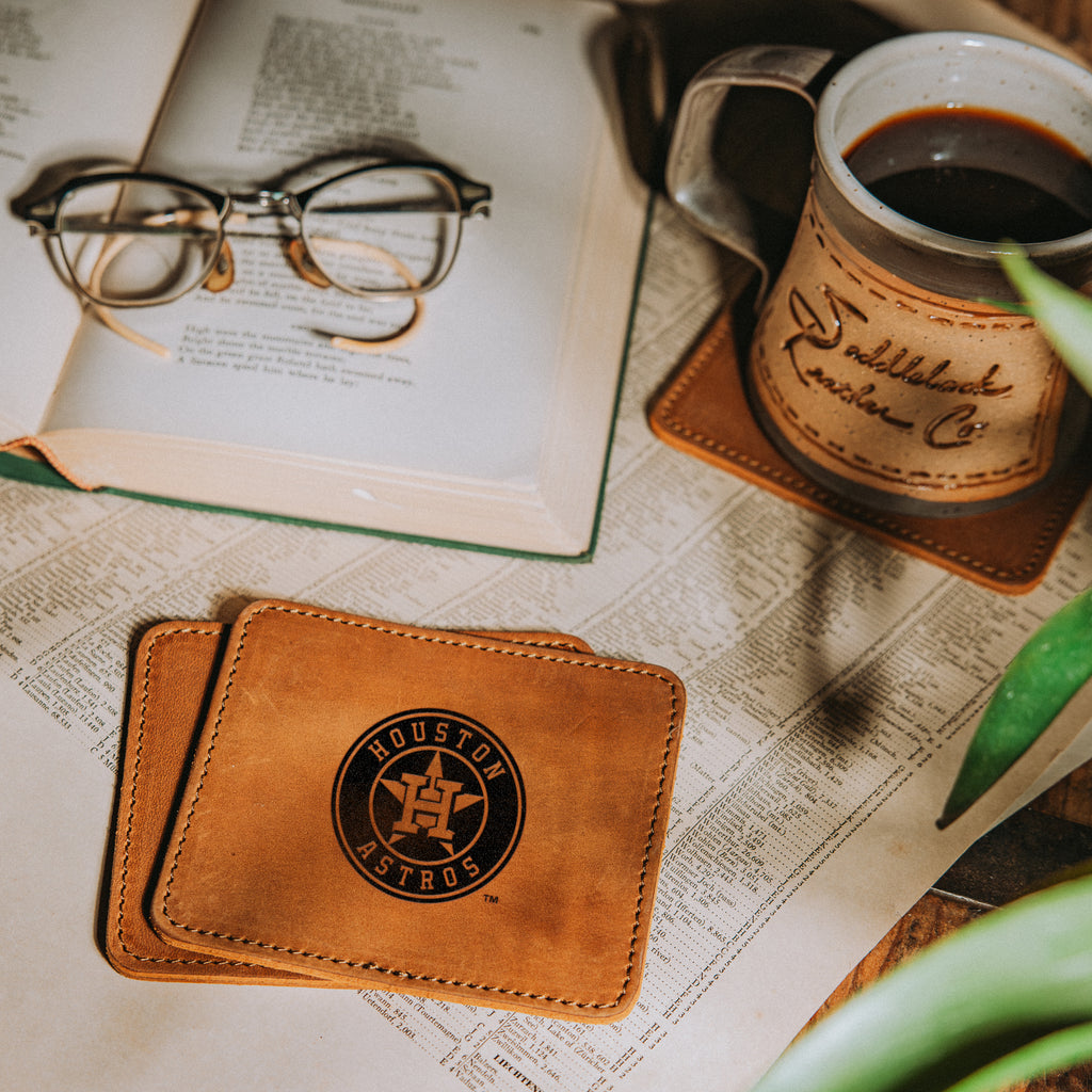 Houston Astros Leather Coaster Set in Tobacco on a table with an open book, glasses and a coffee mug on a coaster