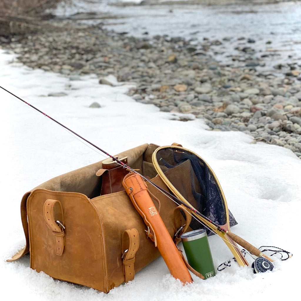 27" Adolescent Beast Duffle Bag in Tobacco in the snow by a river with a fly rod, landing net and tumbler