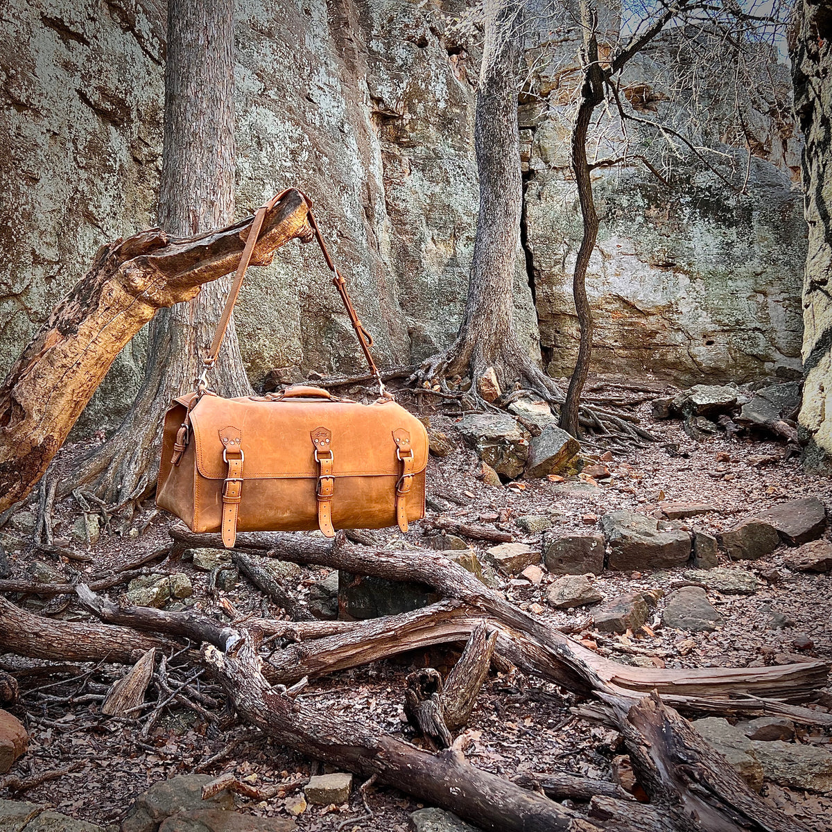 27" Adolescent Beast Duffle Bag in Tobacco on a rocky forest floor among tree roots and boulders