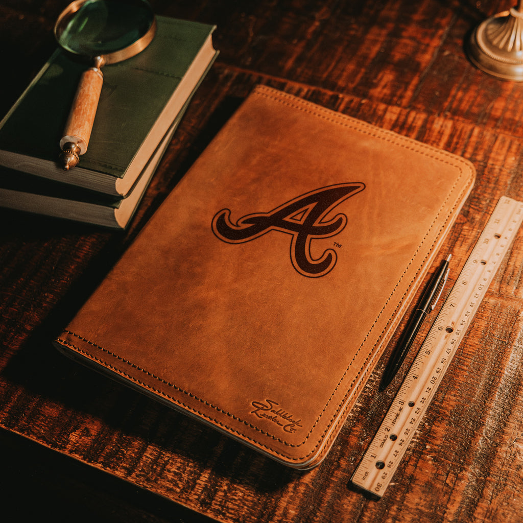 Leather Portfolio - Atlanta Braves in Tobacco on a wooden desk with books, a magnifying glass, pen and ruler