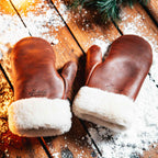 Sheepskin Mittens in reddish brown leather with shearling cuffs, pair on snowy wooden boards