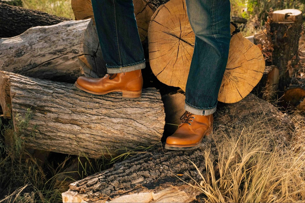 Huntsman Boots - Natural on foot with cuffed jeans, stepping across stacked cut logs in the woods