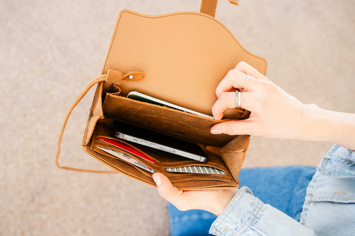 Woman opening the On The Go Leather Wallet in Tobacco to reach a phone and cards inside