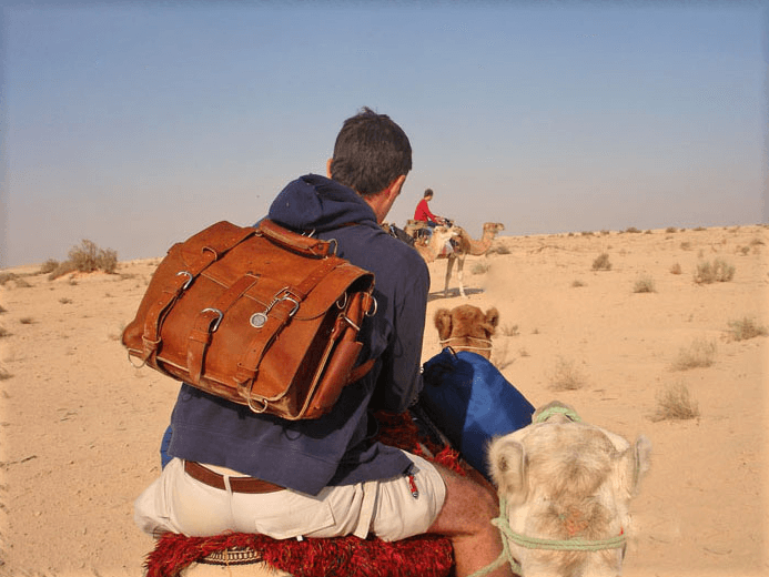 A rider crossing the Sahara on a camel with a Saddleback leather backpack on his back.