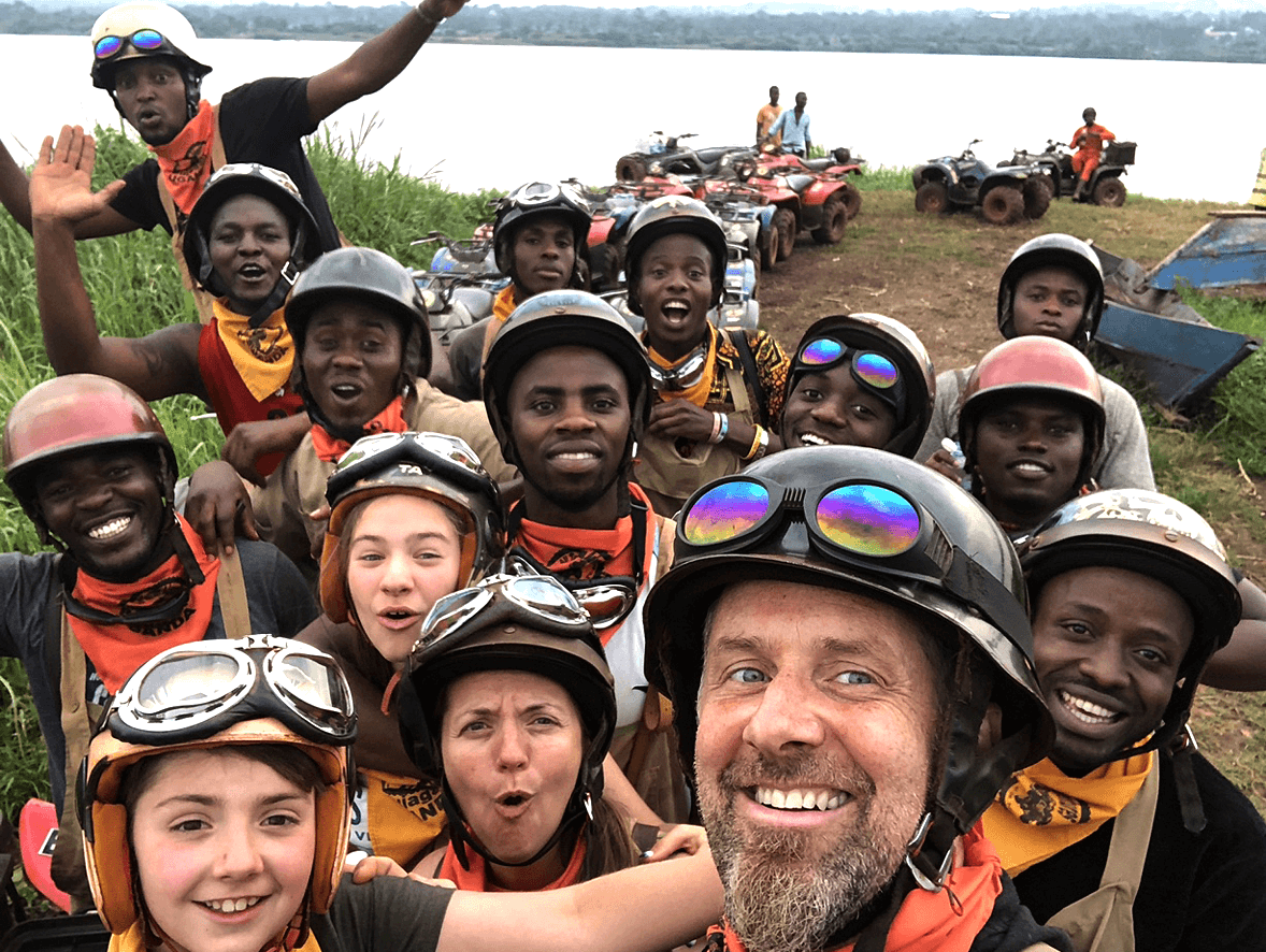 A close group selfie of Dave, Suzette and a crowd of young Rwandans wearing ATV helmets and goggles.