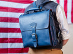 Saddleback Club Membership Paul Revere Leather Messenger Bag Backpack in Red, White and Blue, worn as backpack before a flag