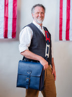 Saddleback Club Membership Paul Revere Leather Messenger Bag Backpack in Red, White and Blue, carried crossbody by a smiling man