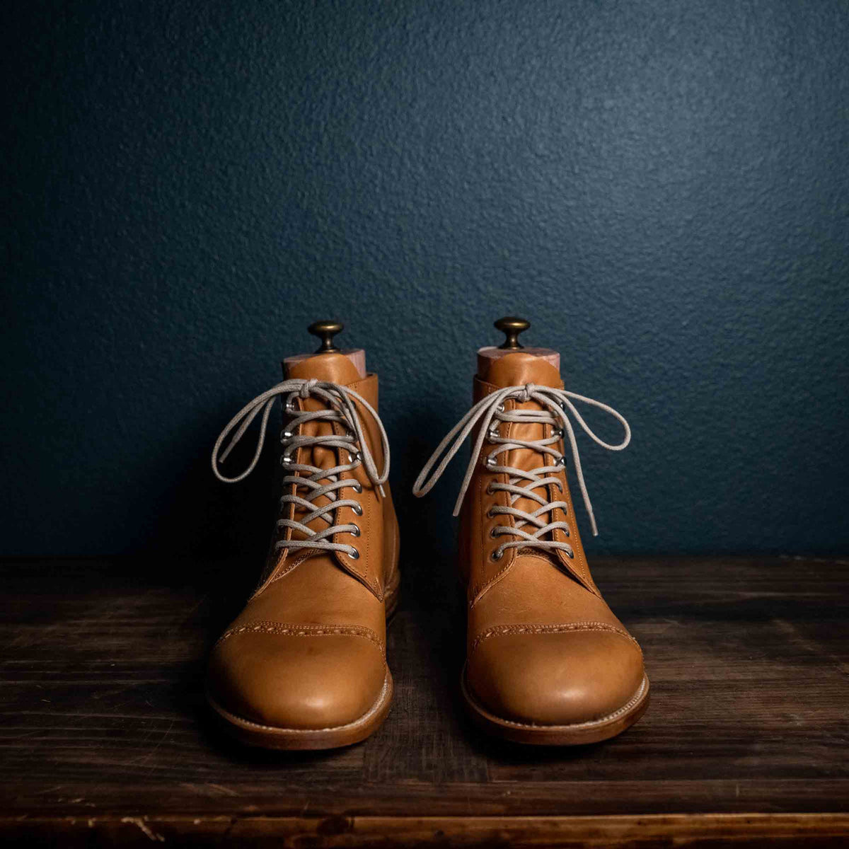 Pair of high quality English tan leather Officer's Boots with light laces on a wooden table, front view