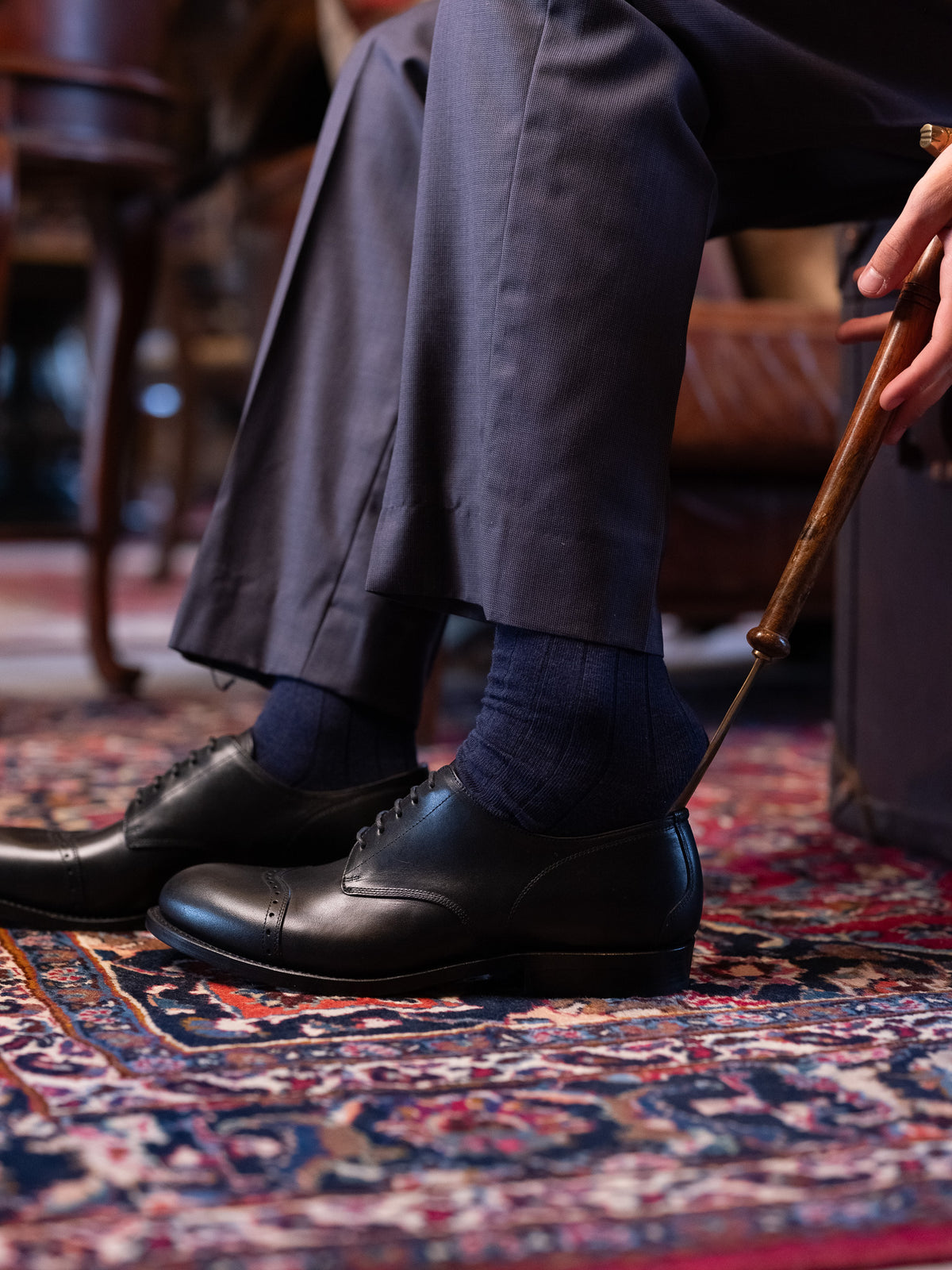 Toe Cap Shoes in Raven Black, slipped on with a long shoehorn over a patterned rug