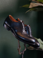 Toe Cap Shoes in Raven Black, pair balanced on an ornate metal stand against a dark green backdrop