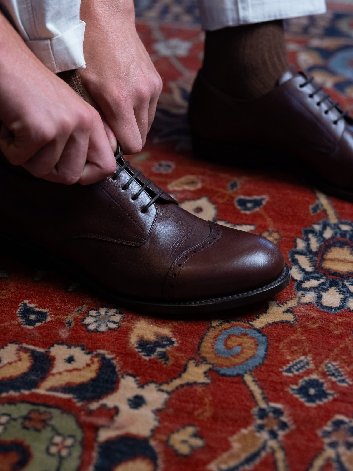 Toe Cap Shoes in Dark Oak, tying the laces on a red patterned rug