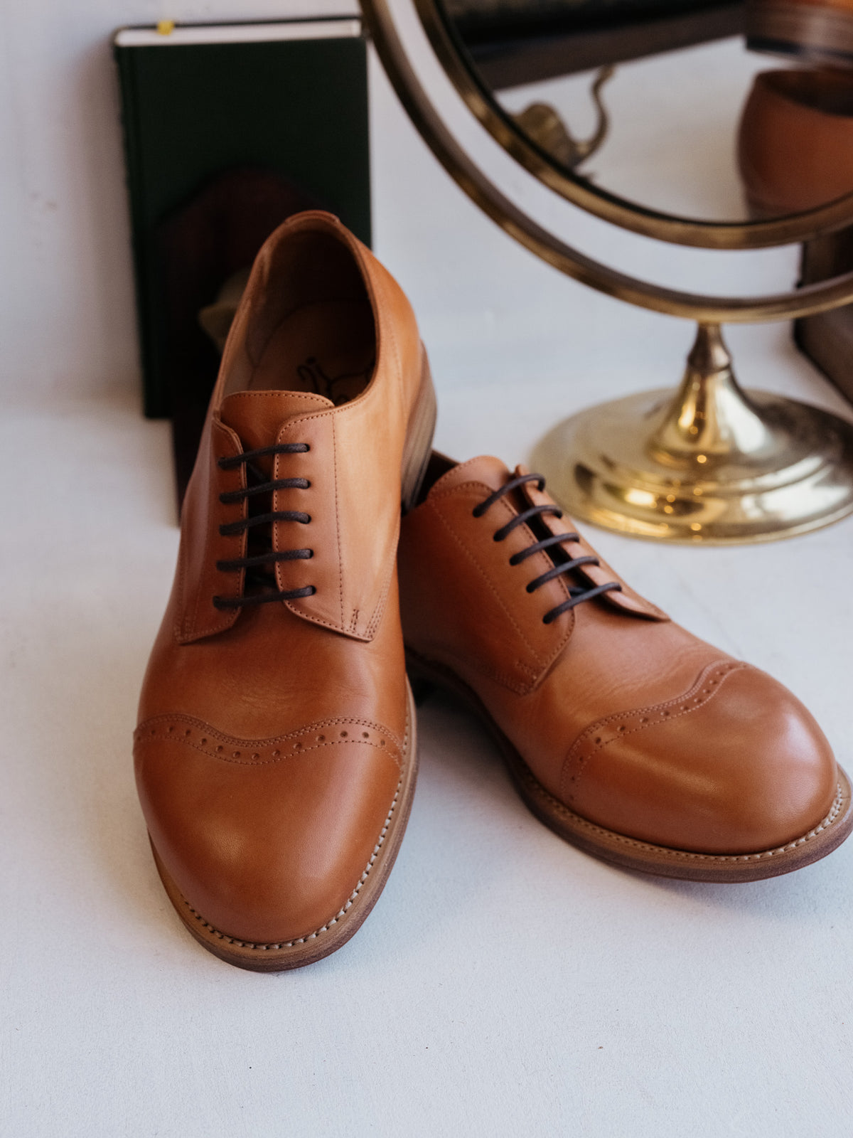 Toe Cap Shoes in English Tan, front three-quarter view of the pair beside a brass mirror and book