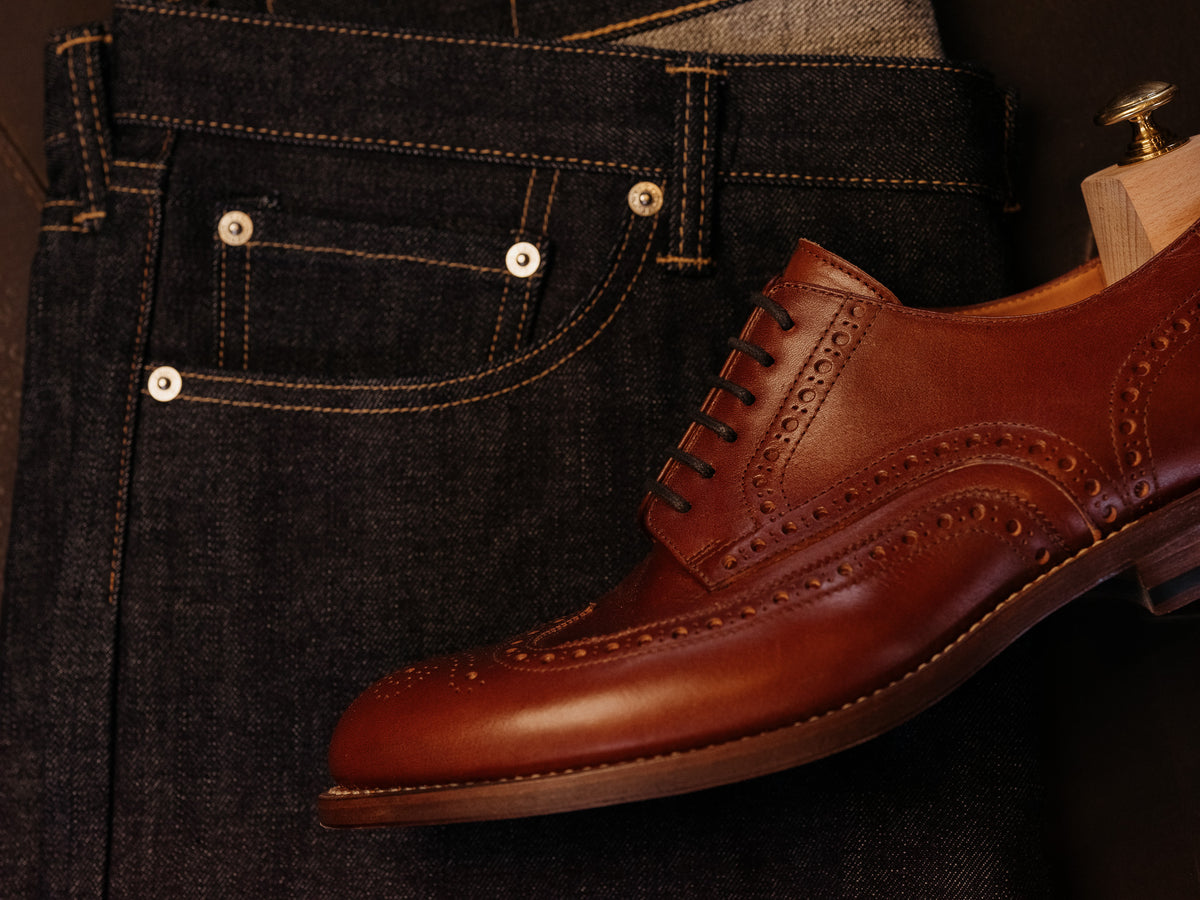Wingtip Shoes in Chestnut, single shoe with shoe tree resting on dark denim jeans