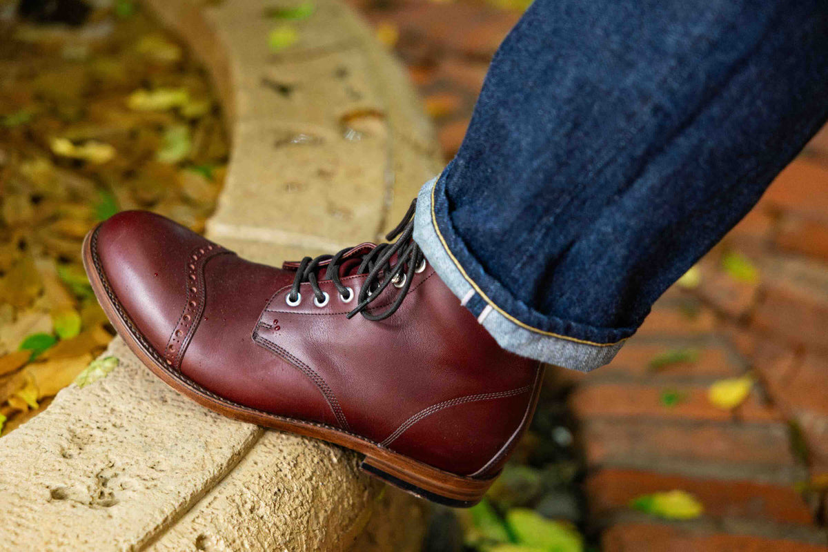 Officer Boot in Oxblood, worn with cuffed jeans on a stone curb among autumn leaves