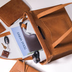 Professional Leather Tote in Tobacco on its side with a book, laptop, keys and leather accessories spilling out