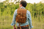 Small Front Pocket Backpack in Tobacco on a man with rolled denim sleeves, rear view in a sunlit grassy field