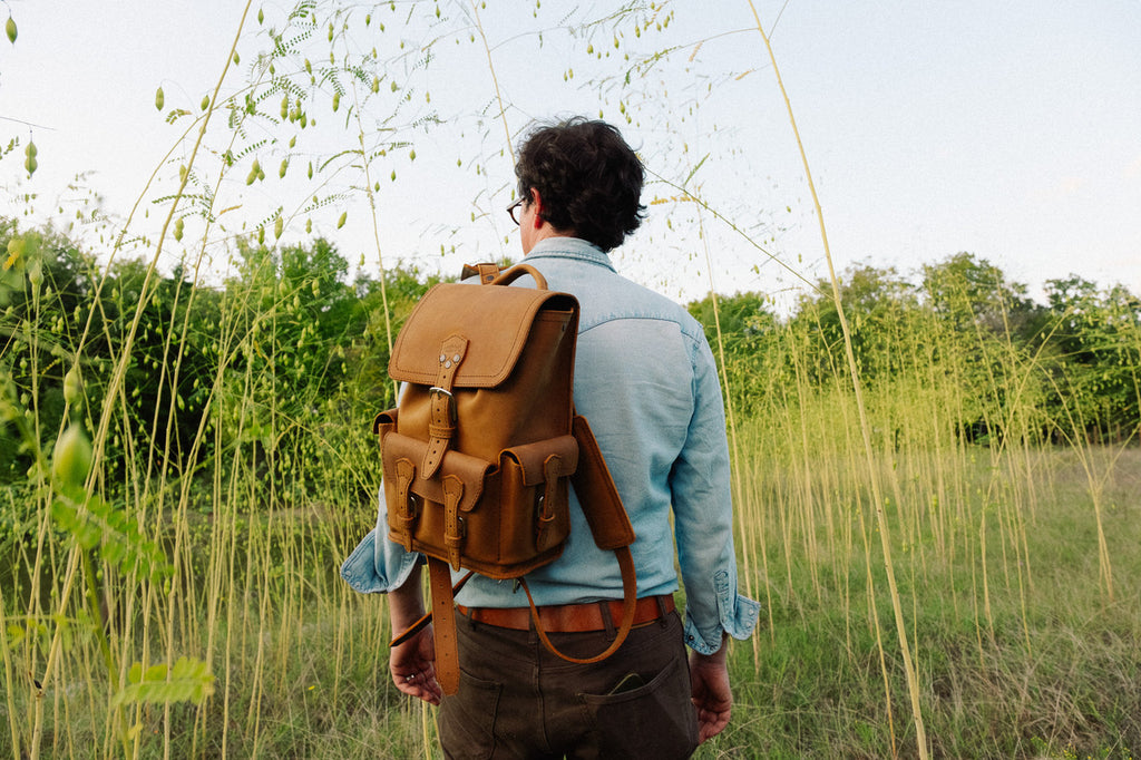 Small Front Pocket Backpack in Tobacco worn by a man facing away across a grassy meadow under a pale sky