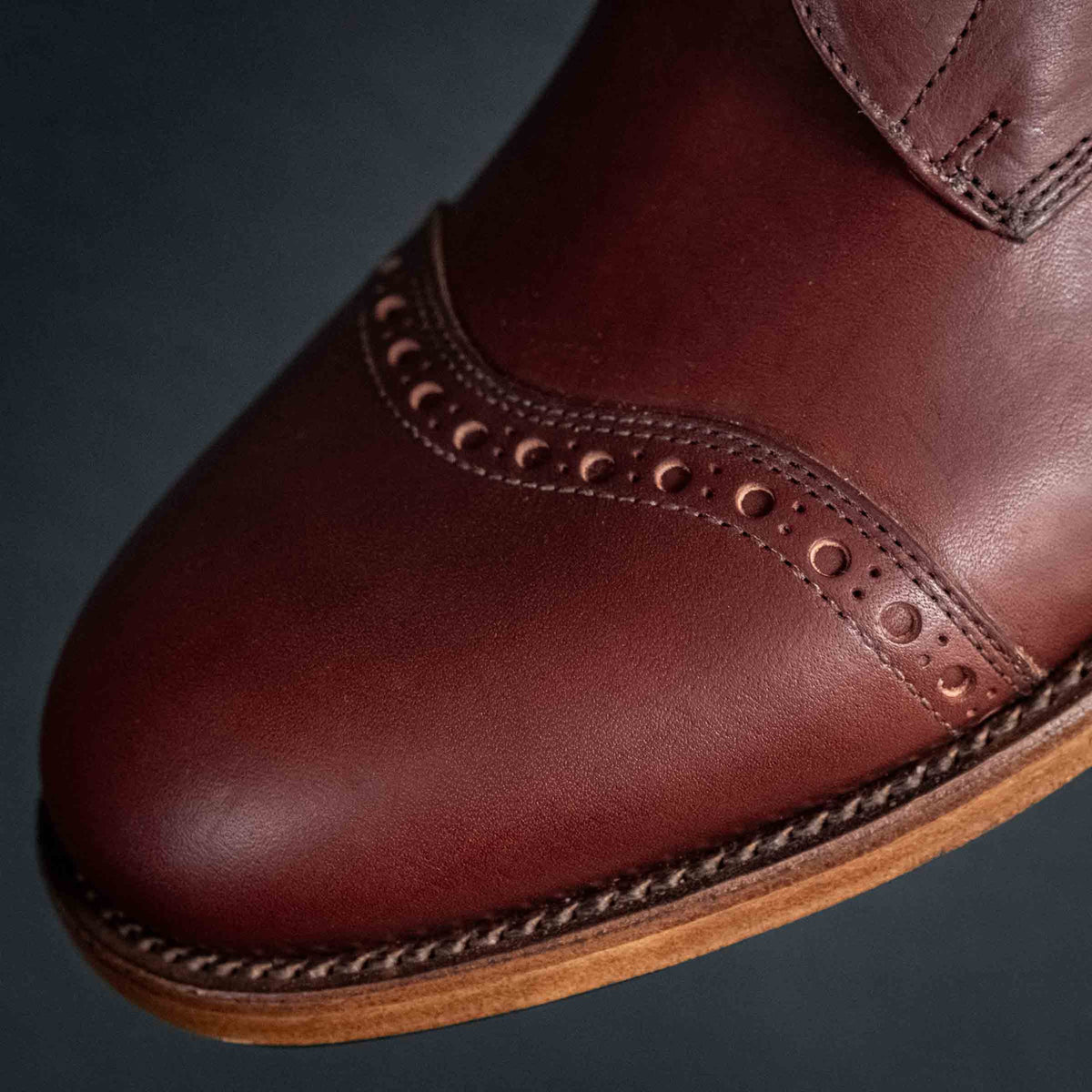 Officer Boot in Oxblood, angled close-up of brogue perforations and stitched welt